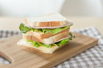 Sandwich with cheese and ham on cutting board on the table in the bright kitchen. Lunch. Sandwich with lettuce. Healthy eating concept.