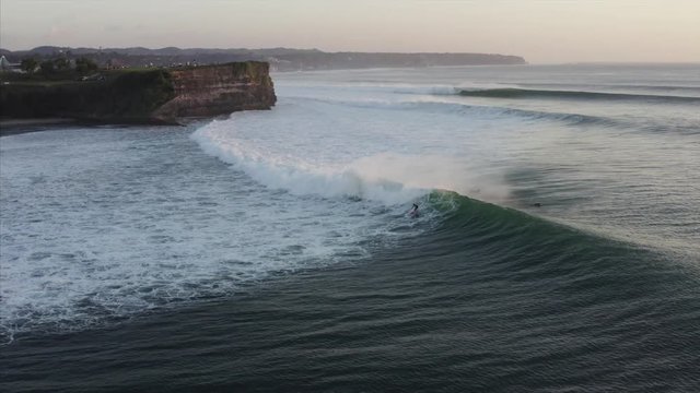 Flying backwards above the ocean, amazing view of foamy waves and surfers of them. Balangan beach in the evening. Bali, Indonesia