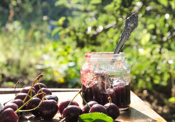 Tasty sweet cherry jam and fresh cherries on the rustic wooden table in the garden
