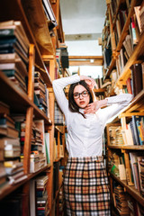 people, knowledge, education and school concept - happy student girl or young woman with book posing in an old library