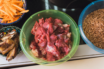 raw meat, carrots, rice and fried bacon in plastic cups. Preparation in cooking pilau in the kitchen