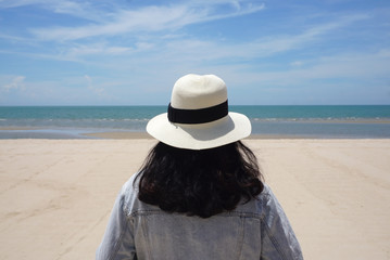 Fototapeta na wymiar Asian woman wearing hat and jeans jacket standing at the beautiful beach looking at the sea