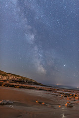 Fototapeta na wymiar Milky Way starscape over beach, rocks and water at night