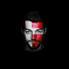 Flag of Denmark painted on a face of a man on black background.