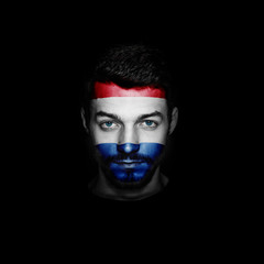 Flag of Netherlands painted on a face of a man on black background.