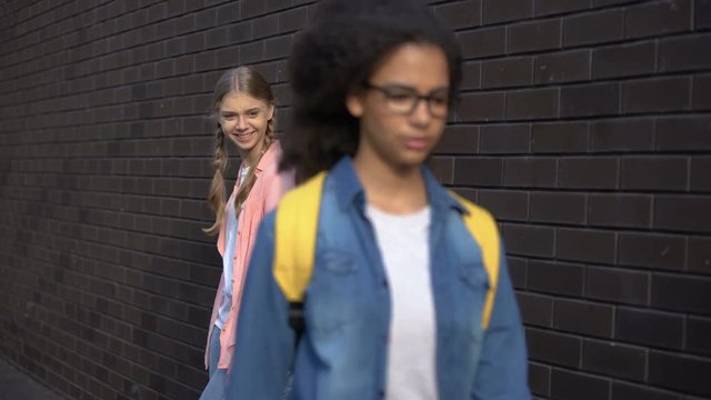 Caucasian teenagers laughing at afro-american schoolmate passing by, racism
