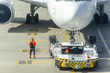 Passenger plane towed by an aircraft towing vehicle on the tarmac of an aerodrome. Aircraft is taxiing to the parking place.Pushback tractor is towing the aircraft to a parking lot. Airport supervisor