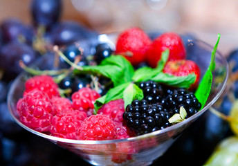 Vase with seasonal fruits and berries. Raspberries, blackberries and mint in a glass bowl.