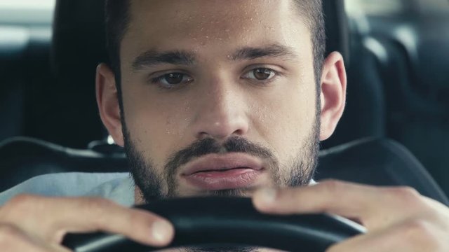 close up of sweaty man gesturing while sitting in car and holding steering wheel 