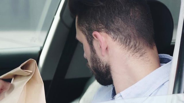 selective focus of window opening near handsome man taking paper bag, holding credit card near seller, paying, and waving hand while sitting in car 