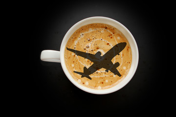 white wide cup of coffee, airplane-shaped cappuccino on a black background with vignette, top view, save space, close-up, concept of travel, transfer