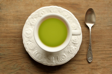 Top view. green tea in a white cup with a saucer and a spoon on a wooden table