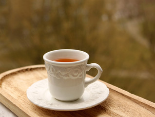 Tea in a white cup with a saucer stands on a light board on a background of greenery
