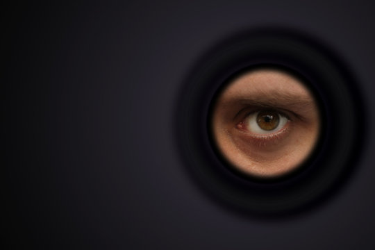 The eye of a man looking out of the eyepiece, the concept of surveillance, peeping, mystery; shot with space for text