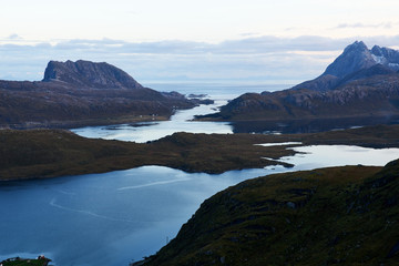 View from above over a bay with snowcapped mountains during evening blue hour on Lofoten Islands in Norway.