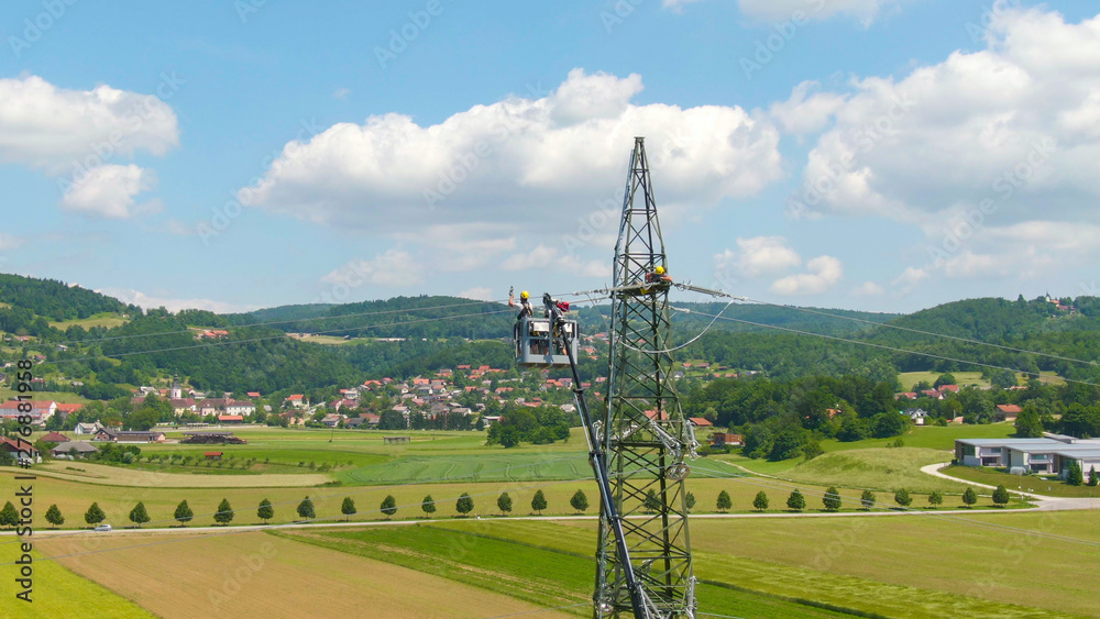 Wall mural drone: electricians on a boom lift lining up high voltage cables on a new tower.