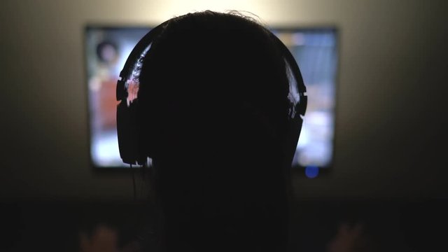 Gamer with Headphones in Dark Room playing Video Game at Night