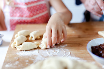 Kid is making croissants with jam. Family is cooking together at home. Dough and ingredients are on kitchen table. Grandmother and child prepare pastries. Children chef concept.
