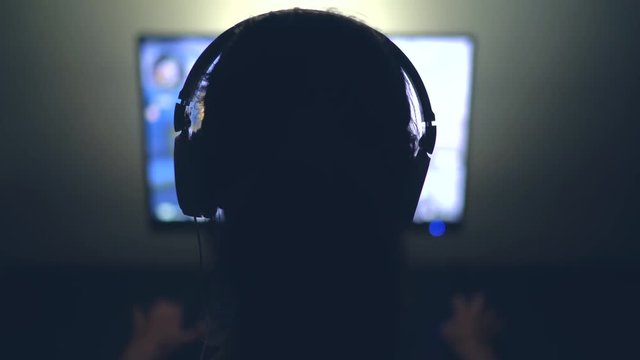 Gamer with Headphones in Dark Room playing Video Game at Night