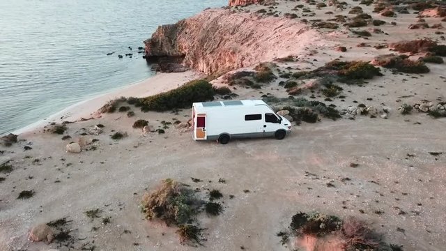 Aerial view of camper van camped above cliff on an epic coastline at sunset