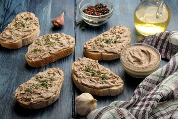 Fresh homemade chicken liver pate with herbs on bread on a blue wooden table. A sandwich.