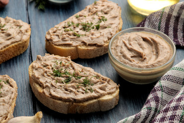 Obraz na płótnie Canvas Fresh homemade chicken liver pate with herbs on bread on a blue wooden table. A sandwich.