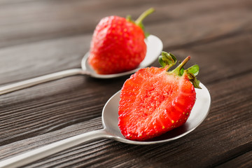 Spoons with ripe strawberry on wooden background, closeup