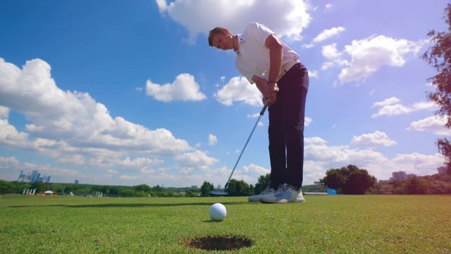 Professional golfer hits a ball into hole on a grass field.