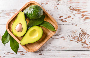 Plate with fresh ripe avocados on white wooden background