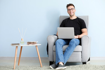 Male blogger with laptop sitting in armchair near color wall