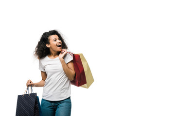 cheerful young curly african american woman holding shopping bags isolated on white