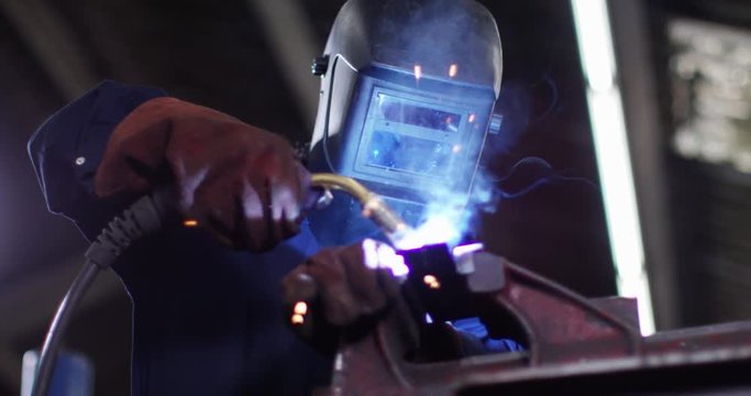 4K Female metalworker in industrial workshop lifting up mask to check her work. Slow motion.