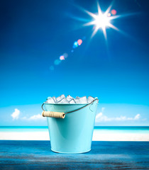 Metal container of ice cubes and beach background. Summer time and sunny day. 