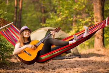 Obraz na płótnie Canvas Woman in hat play guitar and relaxing in hammock in middle of forest. Slow life concept. Hipster.
