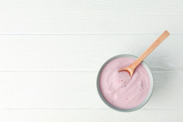 Fruit yogurt in bowl and spoon on white wooden background