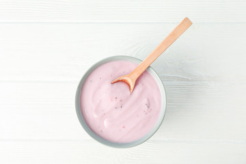 Fruit yogurt in bowl and spoon on white wooden background