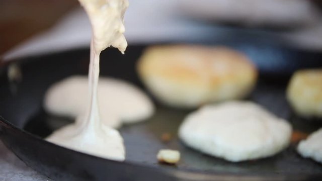 A person making pancakes in the old pan out of the thick dough