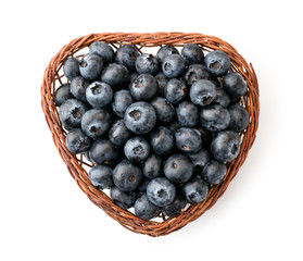 Blueberry berries in a heart shaped basket on a white. The view of the top.