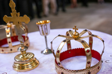 Two crowns and cross on white table prepared for wedding. Orthodox church wedding accessories.