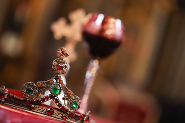 Isolated wedding crown and blurred glass of vine in background. Orthodox church wedding accessories.