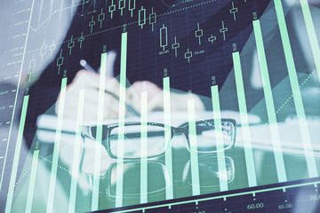Forex chart hologram on hand taking notes background. Concept of analysis. Double exposure