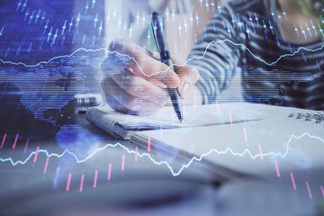 Financial forex graph drawn over hands taking notes background. Concept of research. Double exposure