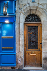 Aged wood door near blue painted framed wall panel with antique lantern of old building in Paris France. Vintage arch doorway and weathered stone wall of ancient house in classical architecture.