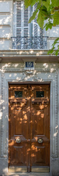 Antique wooden door and shuttered window with ornate balcony of old building in Paris France. Vintage wooden doorway and stucco wall covered with light spots and shadow pattern from tree leaves.