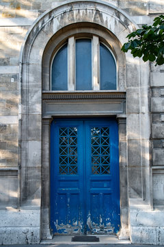 Arch door with window of old building in Paris France. Vintage wooden blue painted doorway with flaking paint and weathered grey stone wall of ancient house in classical architecture near Notre-Dame