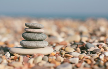 Fototapeta na wymiar Stone zen pyramid on blurred beach background. Warm summer photo. Calm and rest place. Spa therapy background. Text space.
