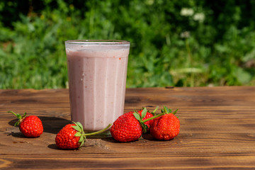 Glass of fresh strawberry smoothie on a wooden table outdoor