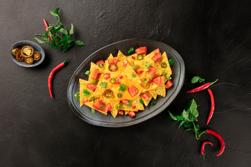 Mexican nachos, shot from the top with a cheese sauce, chili and jalapeno peppers, tomatoes, and cilantro, on a black background with copy space