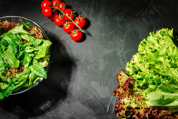 Fresh green salad with spinach, arugula, romaine and lettuce in a glass bowl on dark background