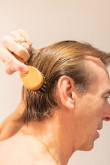Homme aux cheveux blonds démélant ses cheveux en les brossant - obrazy, fototapety, plakaty